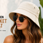 A stylish outdoor fashion portrait of a young woman wearing a cream women bucket hat and sunglasses, showcasing a modern trendy look with soft natural lighting and a blurred green background.